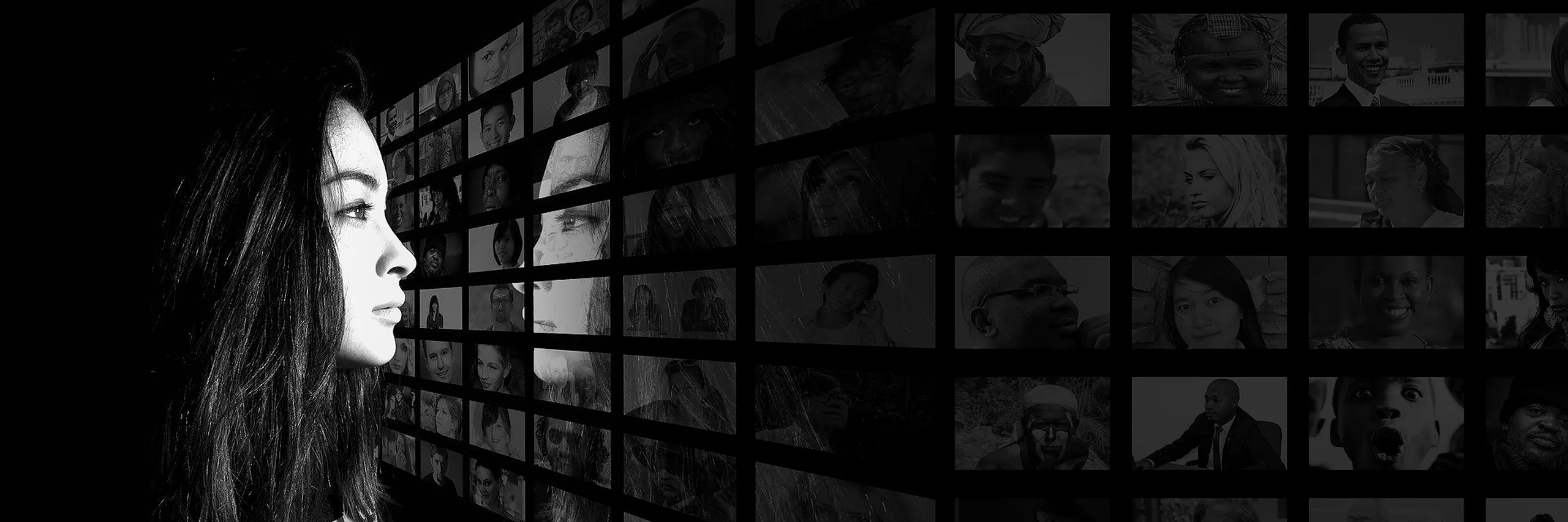 A woman in profile, lit against darkness, observing a wall of audience portraits
